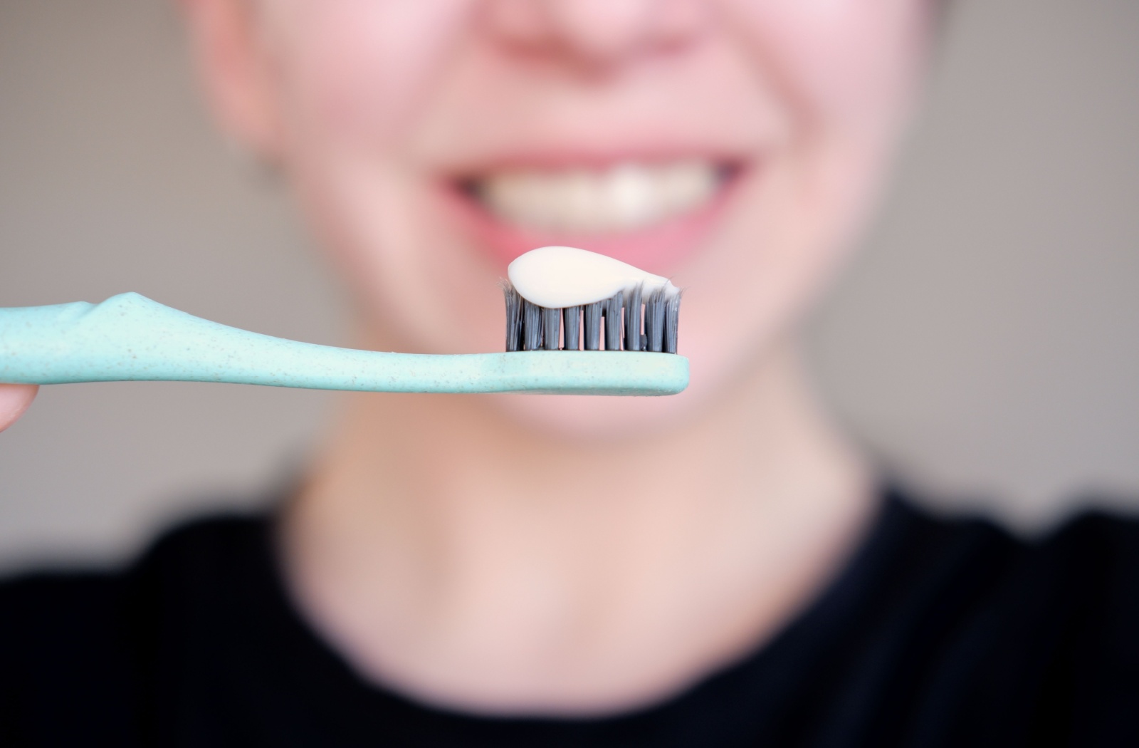 Close-up of a toothbrush with toothpaste as a person smiles in the background.